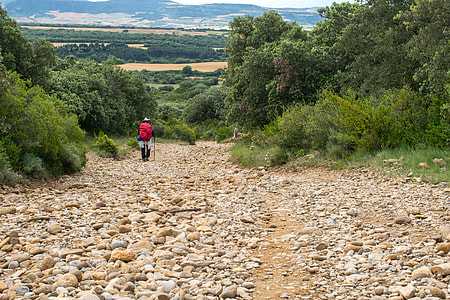 man wearing red backpack hiking walking on road with rocks thumbnail