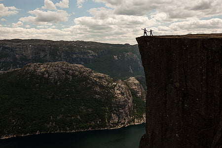 two person standing near cliff under blue and white cloudy sky during daytime thumbnail