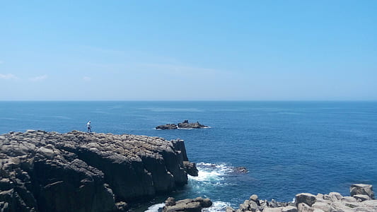 person walking on rock formation near sea at daytime thumbnail