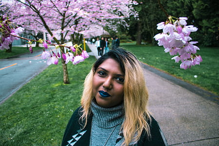 Smiling Woman Standing on Sidewalk Beside Road Near Pink Cherry Blossom Tree thumbnail