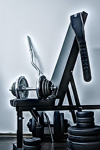 gray barbell and blue gym belt placed on black and gray exercise bench near wall thumbnail