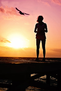 silhouette of woman near shore during sunset thumbnail