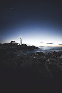 white lighthouse near body of water under starry sky thumbnail