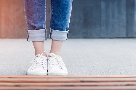 person wearing pair of white sneakers standing on concrete pavement thumbnail