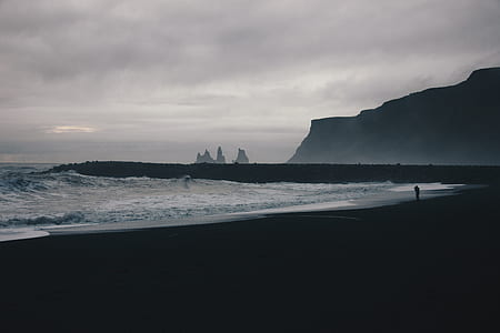 silhouette photo of person walking on shore near mountain thumbnail