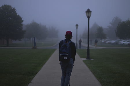 person wearing black jacket and blue pants standing on concrete pathway thumbnail