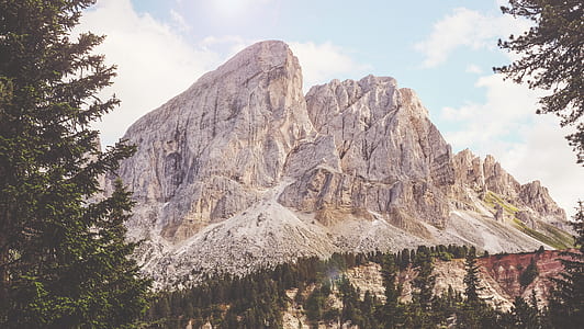 landscape photography of white rocky hill near green leaf trees under blue cloudy sky thumbnail