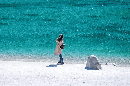 woman standing on white sand near body of water during daytime thumbnail