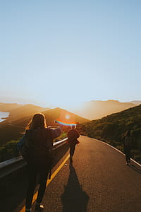 three people walks through road near mountain under blue sky during sunset thumbnail