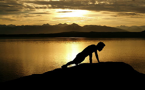 Silhouette of man doing pushups on the beach at sunset. thumbnail