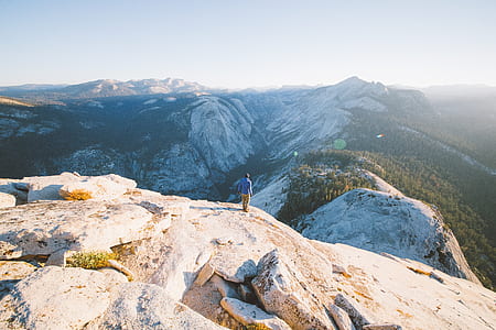 man in blue long-sleeved shirt standing on mountain cliff thumbnail