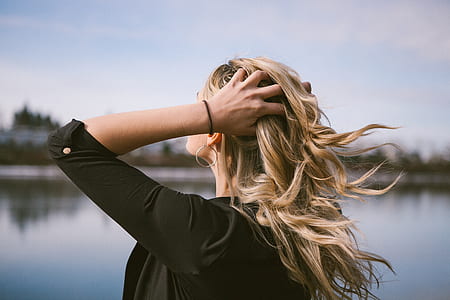 woman in black top touching hair hair in front of body of water thumbnail