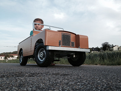 boy riding brown vehicle ride-on toy on road thumbnail