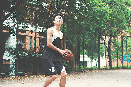 man holding brown basketball near gray metal fence thumbnail