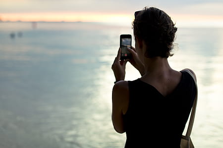 woman using smartphone standing in front of body of water thumbnail