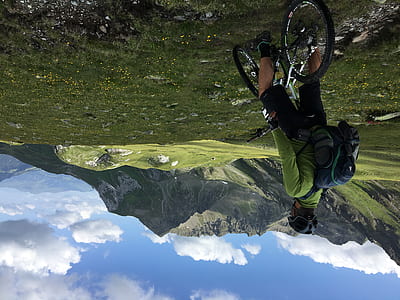 man riding a gray mountain bike watching green grass field and gray mountains under cloudy sky during daytime thumbnail