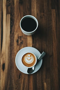 top view photography of white ceramic mug with creamy latte coffee near brewed coffee on brown wooden table thumbnail
