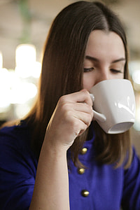woman wearing blue top drinking from white ceramic mug thumbnail