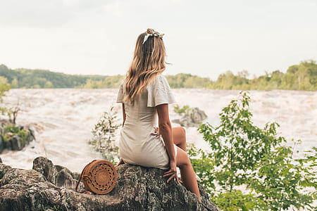 photo of woman sitting on rock near body of water thumbnail