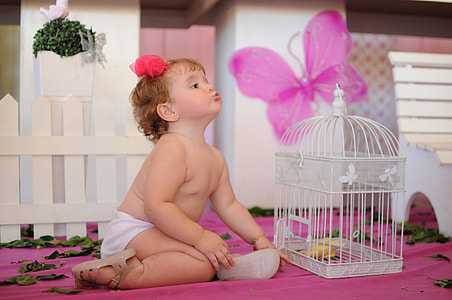 baby's white bottoms beside white metal birdcage on pink surface thumbnail