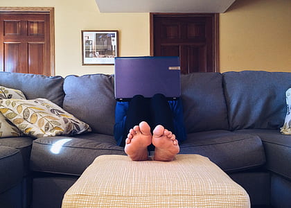 person wearing black pants sitting on gray sofa with purple laptop on lap thumbnail