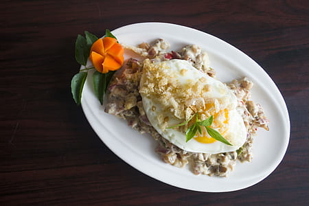 Serving of Marinated Meat With Sunny Side-up Egg and Slice of Carrot in Oval White Ceramic Plate thumbnail