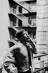 grayscale photo of men holding cigarette standing near concrete building thumbnail