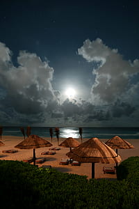 four brown beach umbrellas near blue body of water under nimbus clouds at daytime thumbnail