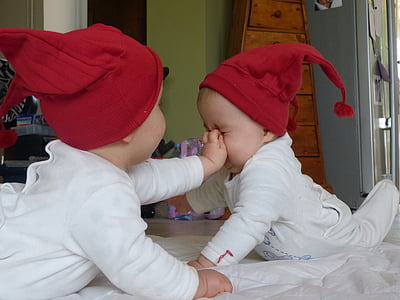 baby pushing the nose of the baby in front of him while crawling on white comforter thumbnail