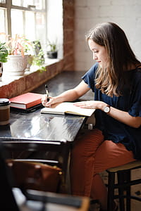 woman sitting and writing on book near the window thumbnail