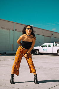woman wearing black tube top and brown pants standing on brown pavement thumbnail