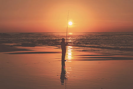 silhouette photo of person fishing on shore under dawn thumbnail
