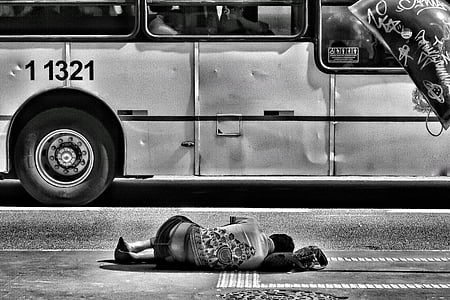 grayscale photo of man laying on street near bus thumbnail