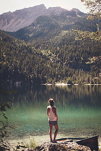 woman standing on a rock looking at body of water and a mountain thumbnail