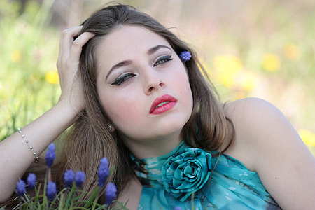 women in teal halter-top dress lying near purple petaled flower in focus photography during daytime thumbnail