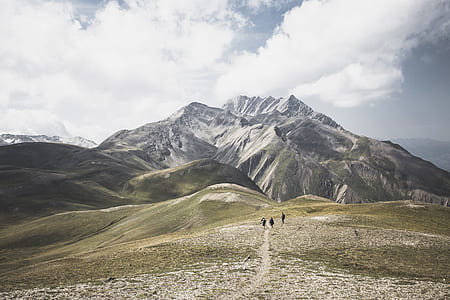 three people walking on pathway infront of mountains under white clouds during daytime thumbnail