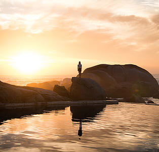 water mirror reflection of woman standing on rock during sunrise thumbnail