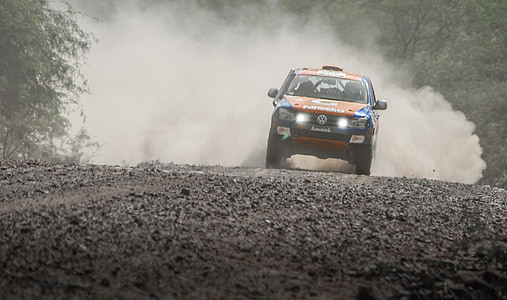 orange and black vehicle traveling on dirt road during daytime thumbnail