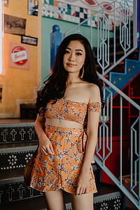 selective focus photography of woman wearing off-shoulder bustier top and rompers outfit standing at staircase thumbnail