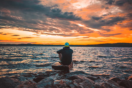 man sitting on stone in the middle of sea thumbnail