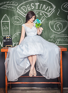 woman wearing grey satin sleeveless ball gown holding blue and white hydrangea flowers bouquet sitting on brown wooden table beside chalkboard thumbnail