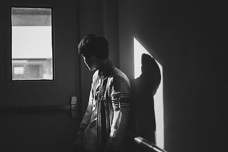 grayscale photography of a man leaning on wall looking at window thumbnail