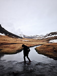 person walking on river near brown mountain range during daytime thumbnail