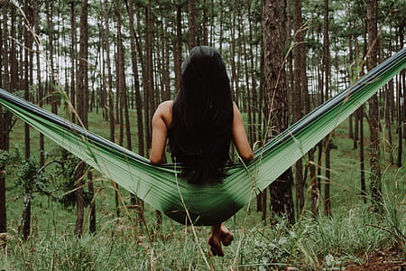 woman sitting on hammock swing facing trees thumbnail