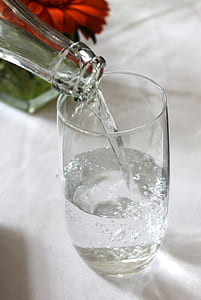 clear glass bottle pouring clear liquid into clear drinking glass thumbnail