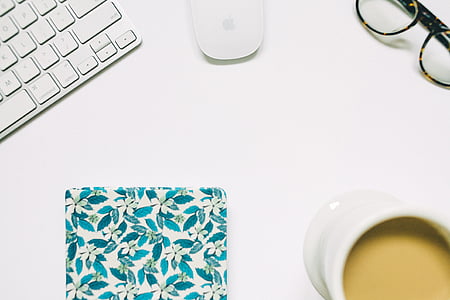 flat lay photography of coffee cup beside cloth, Apple keyboard, Magic Mouse, and eyeglasses thumbnail