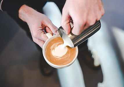 person holding white ceramic mug with coffee mixing milk thumbnail