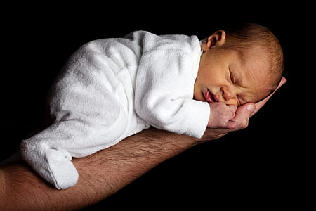Baby in White Onesie Sleeping on Person's Hand thumbnail