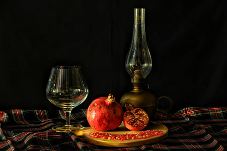 pomegranate between wine glass and oil lamp on table thumbnail