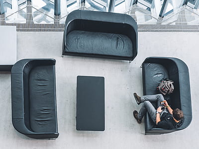top view photography of man sitting on gray loveseat beside bag thumbnail